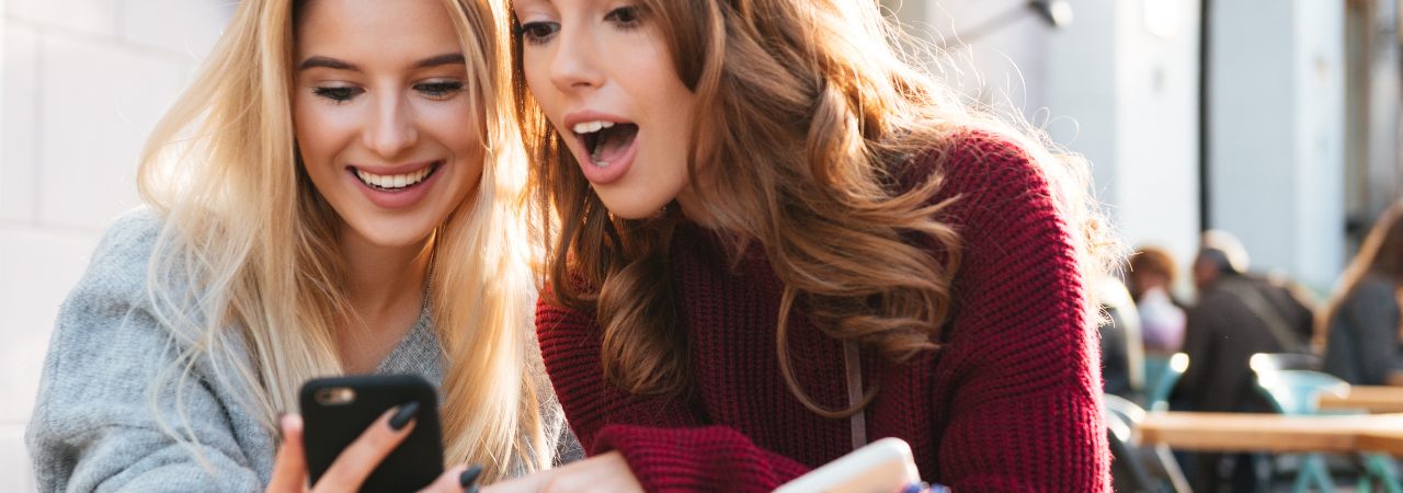 Two friends reading a magazine on a phone at a café table